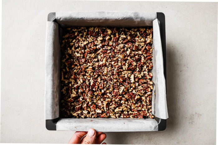 pecan pie brownies in a parchment-lined square baking pan, topped with chopped pecans.
