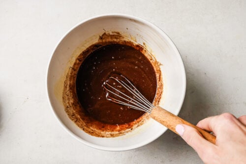 Rich pecan pie brownie batter in a white mixing bowl, ready to be poured into the pan for baking.