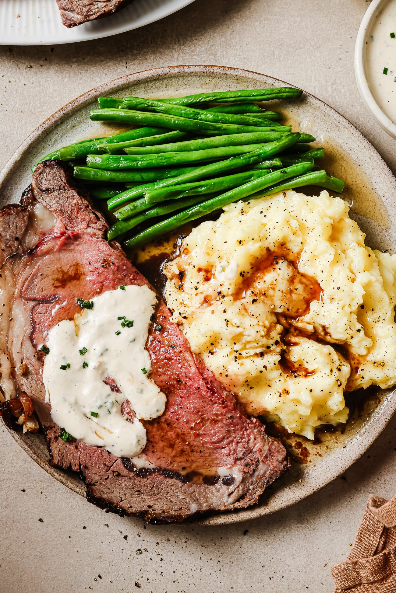 Juicy slices of reverse sear prime rib served with mashed potatoes, green beans, and horseradish sauce on a plate. A perfect holiday dinner.