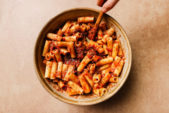 Mixing ground meat sauce with pasta in a bowl.