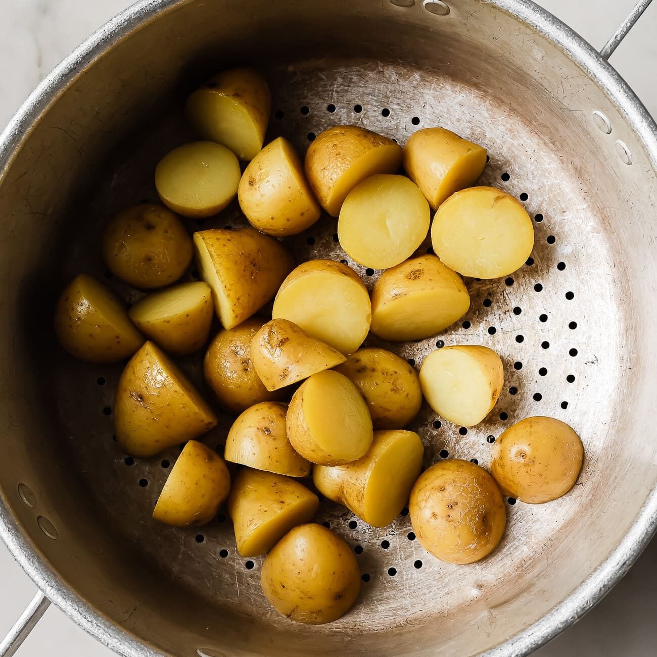 An overhead view of baby potatoes draining in a pot.