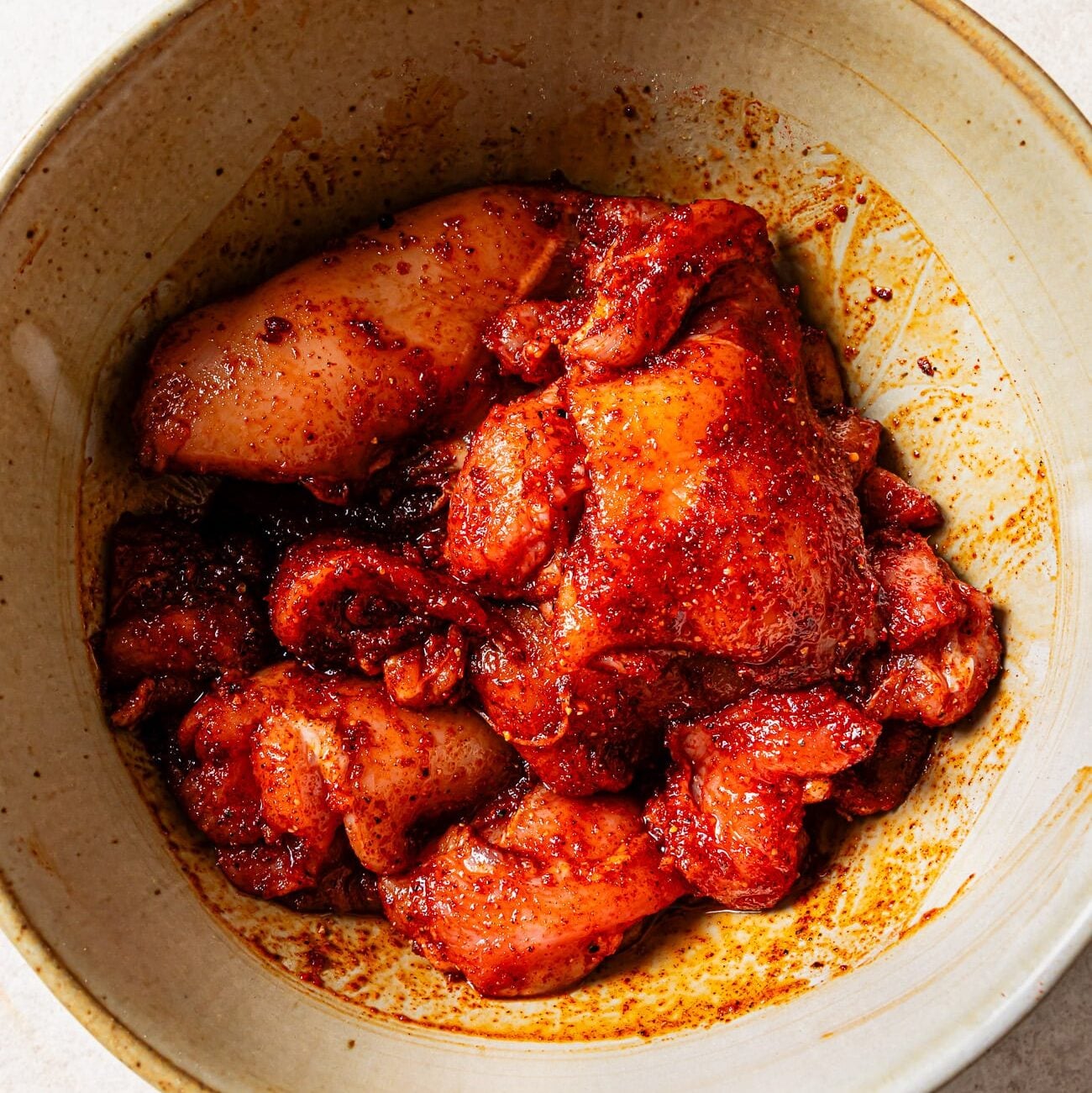 Raw, seasoned chicken thighs in a bowl