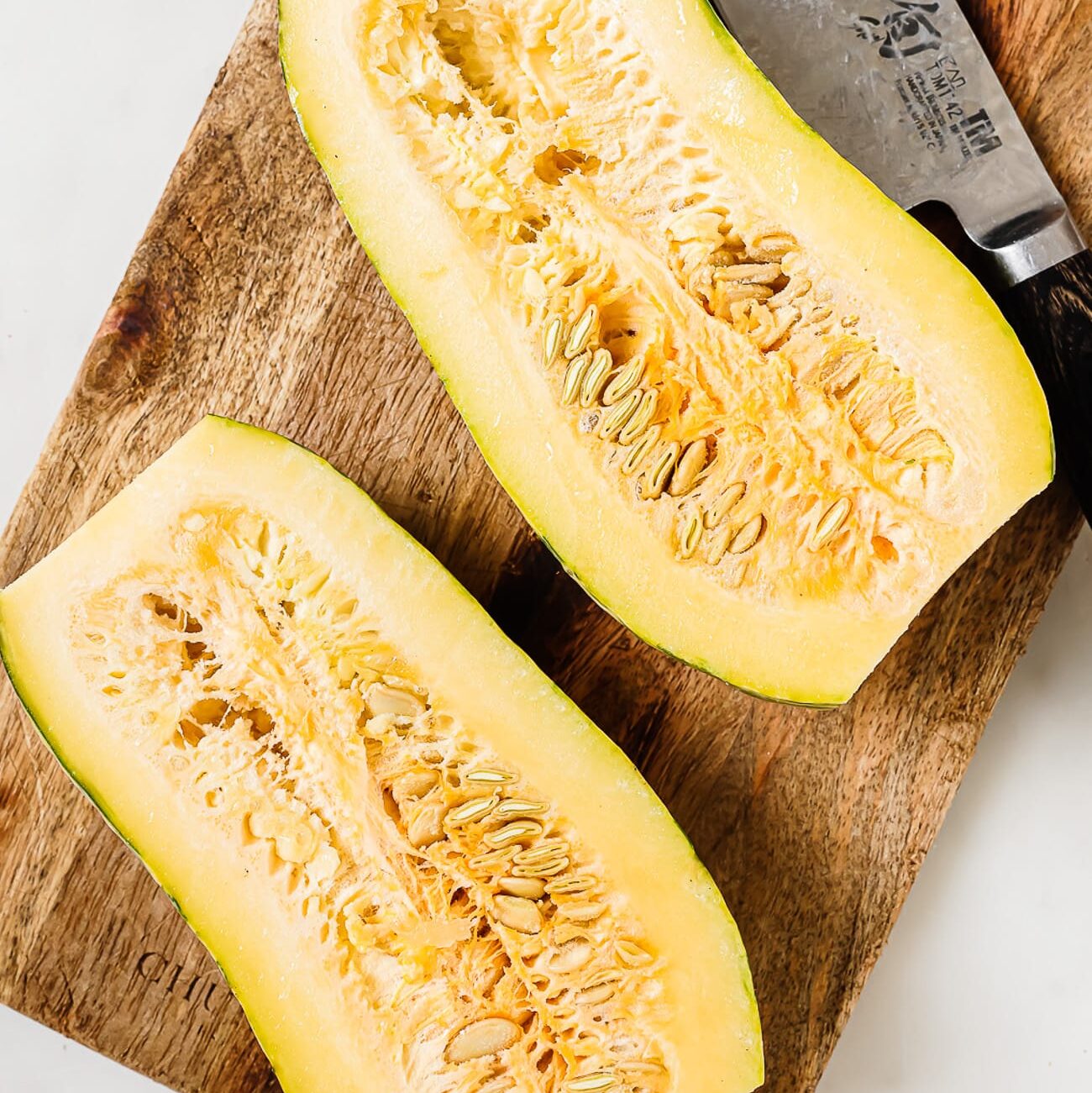 A delicata squash cut in half on a wooden cutting board.