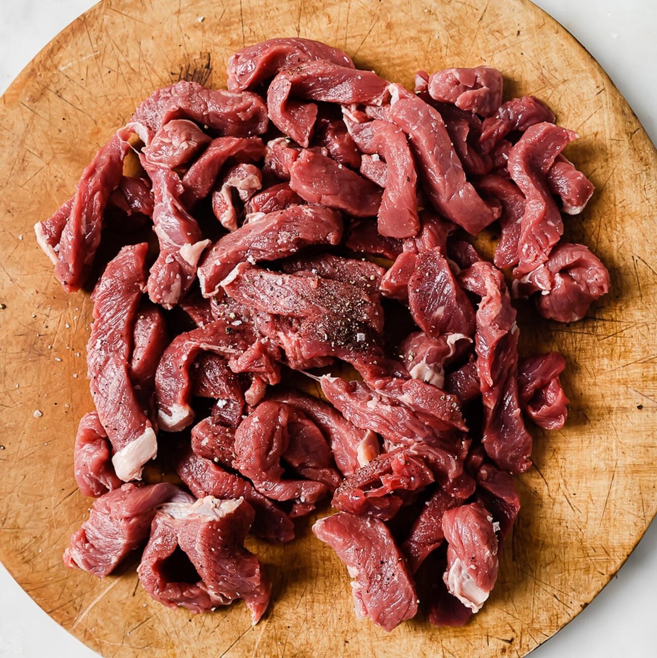 Seasoned sirloin strips on a wooden cutting board.